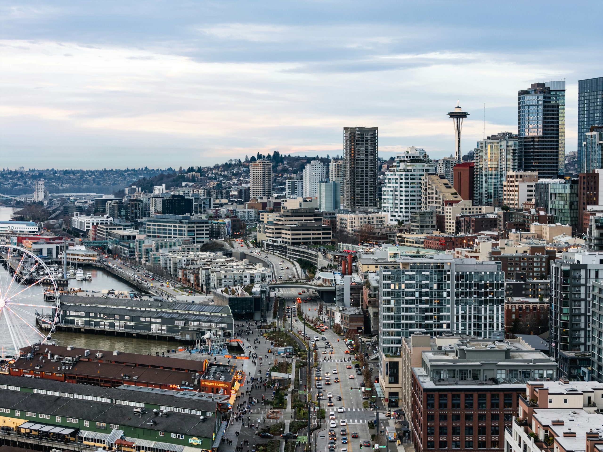 Aerial view of the Seattle waterfront, including the Great Wheel, Miners Landing, and the Space Needle in the distance.
